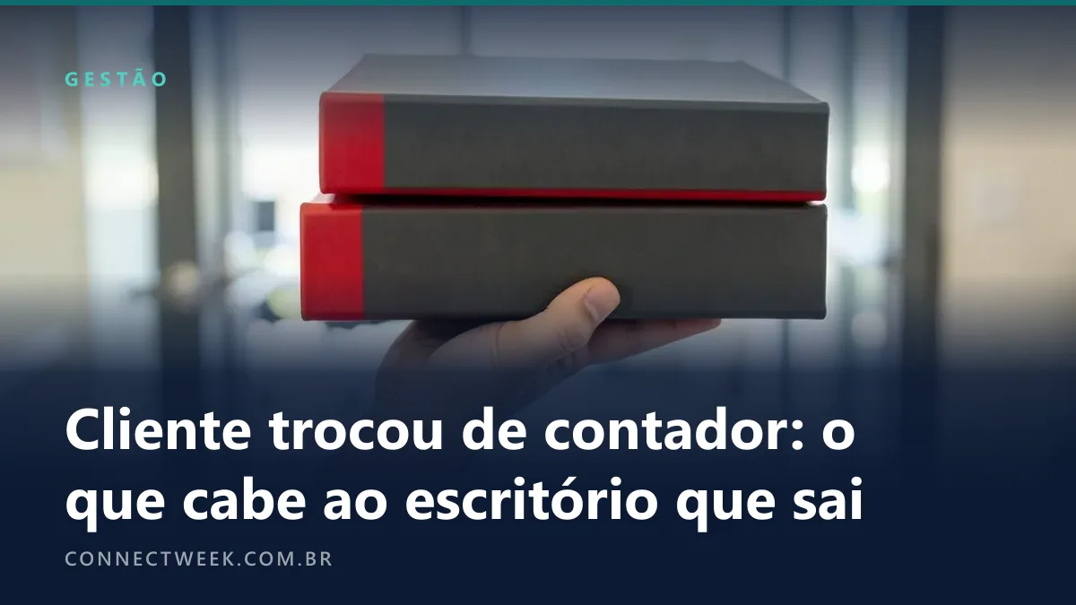 Mão erguendo dois livros grossos de capa dura cinza com lombada vermelha, com um corredor de escritório desfocado ao fundo