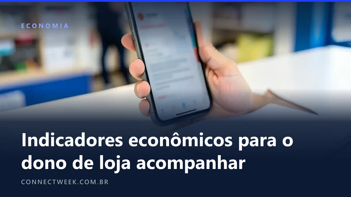 Mão de lojista segurando um celular com página de notícias econômicas desfocada ao lado de um caderno pautado em branco no balcão
