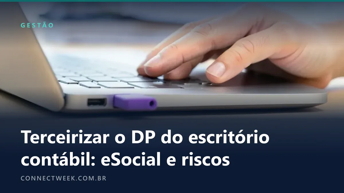 Pen drive roxo conectado à lateral de um notebook prateado, com uma mão apoiada sobre o teclado