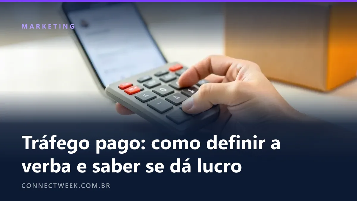 Mão segurando uma calculadora sobre a mesa onde um celular mostra painel de anúncios desfocado e um pacote espera ao lado